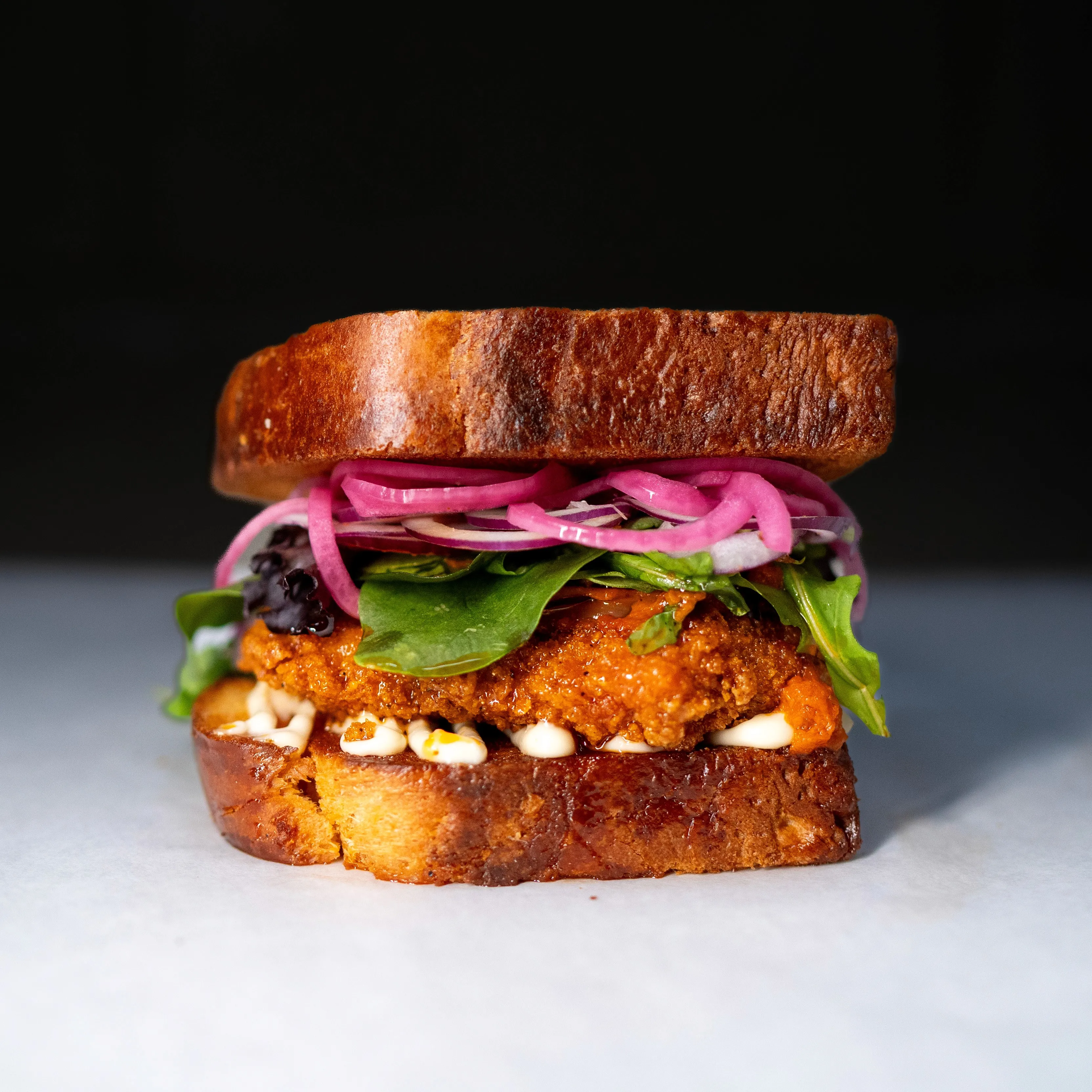 Macka med friterad kyckling, mixsallad och picklad rödlök på brioche