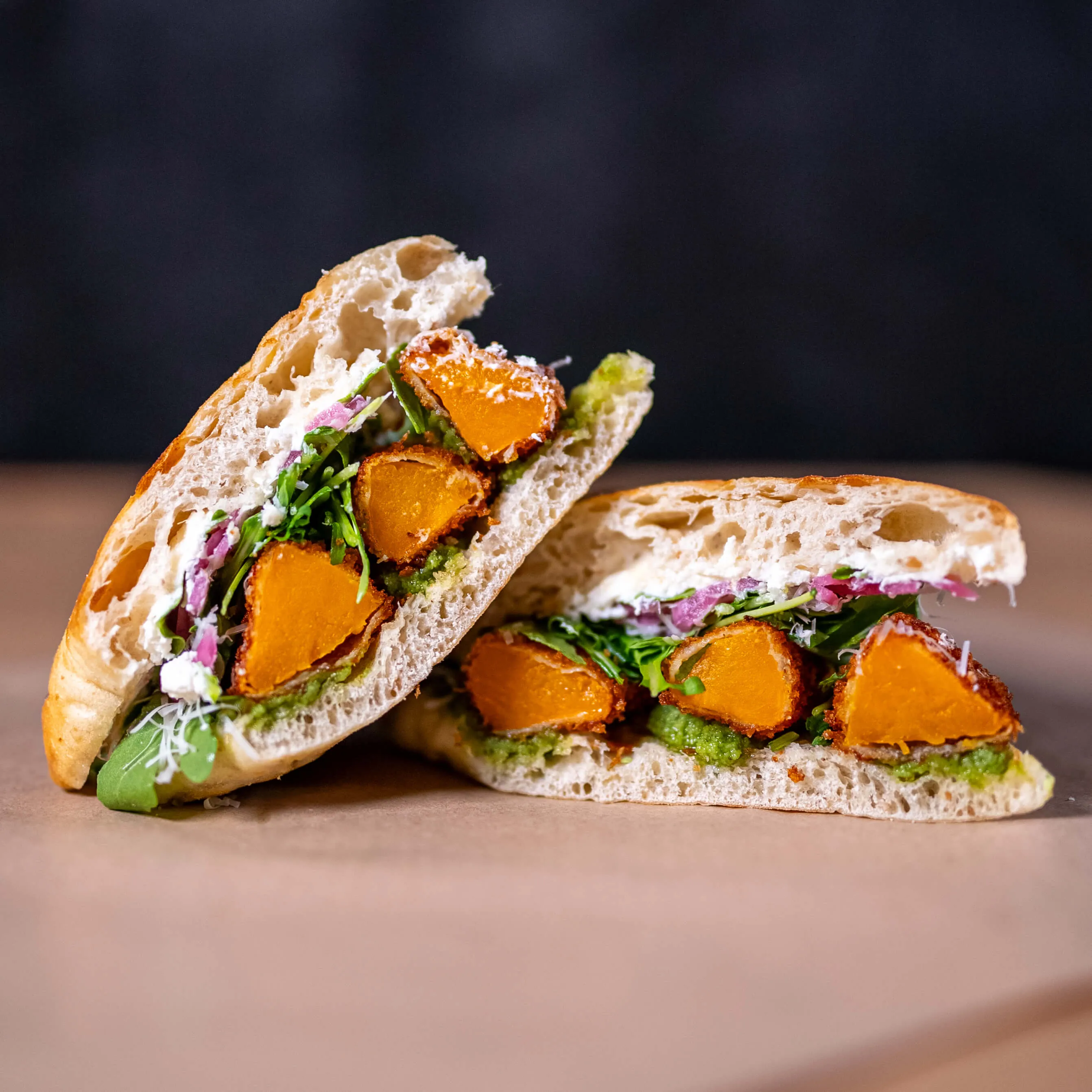 Vegetarisk macka med friterad pumpa, pesto och picklad rödlök i genomskärning